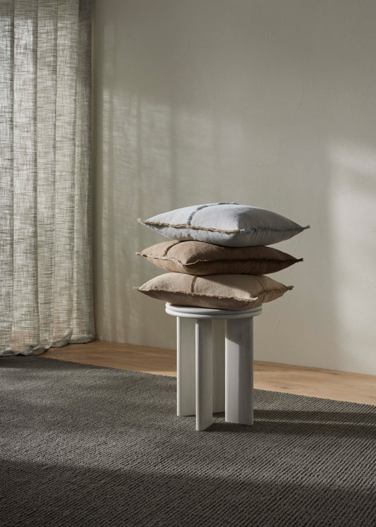 Stack of pillows on a small pedestal against a neutral wall with curtains.