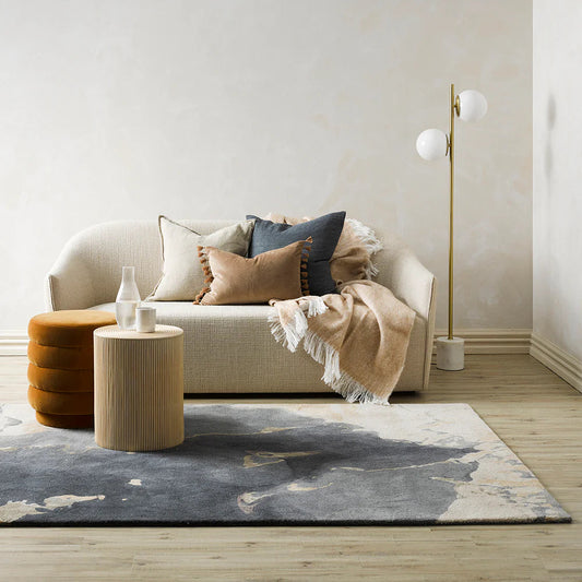 Modern living room with a beige sofa, brown ottoman, and decorative pillows.