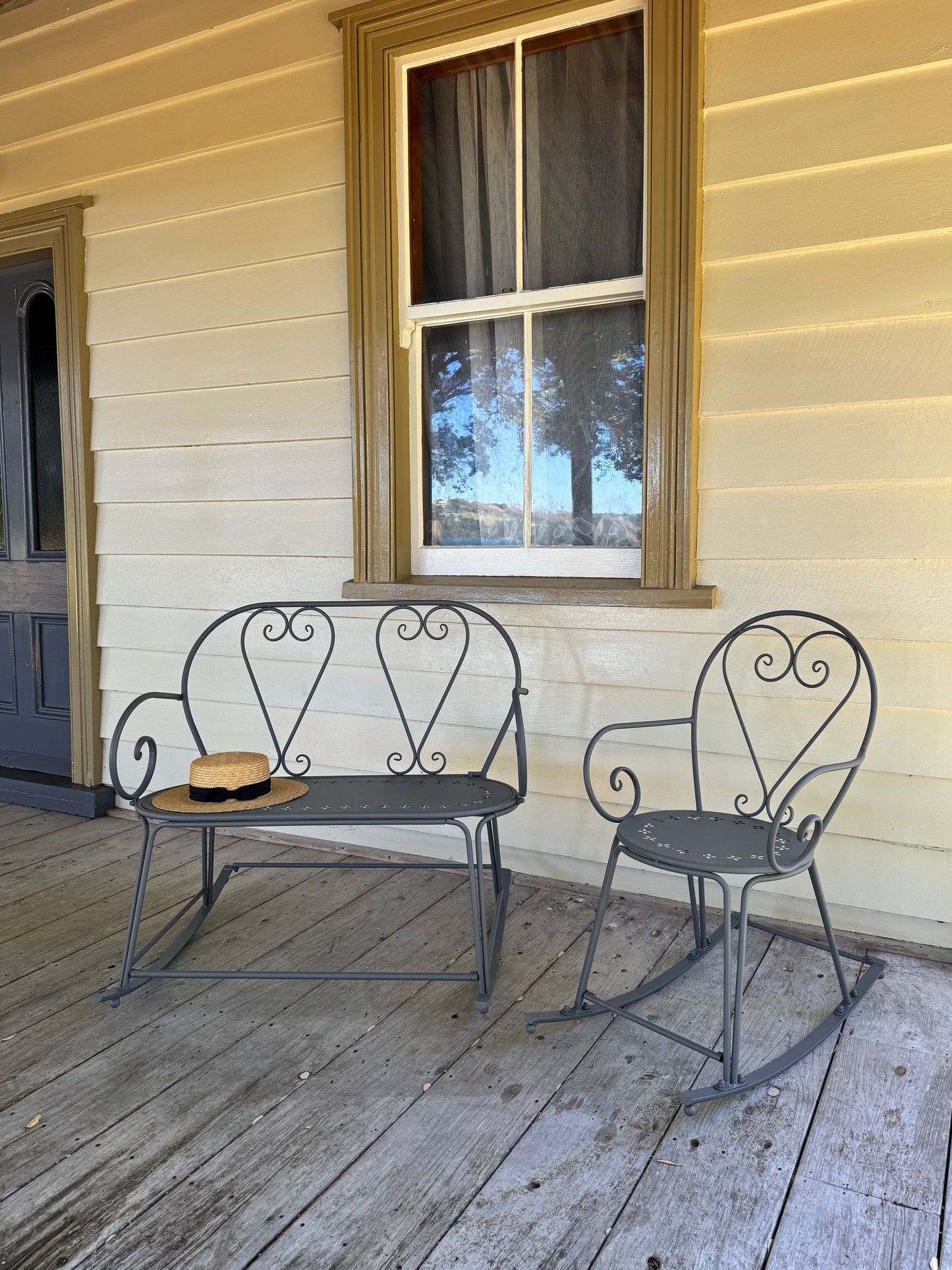 Wrought iron bench and chair on a wooden porch with a window in the background.