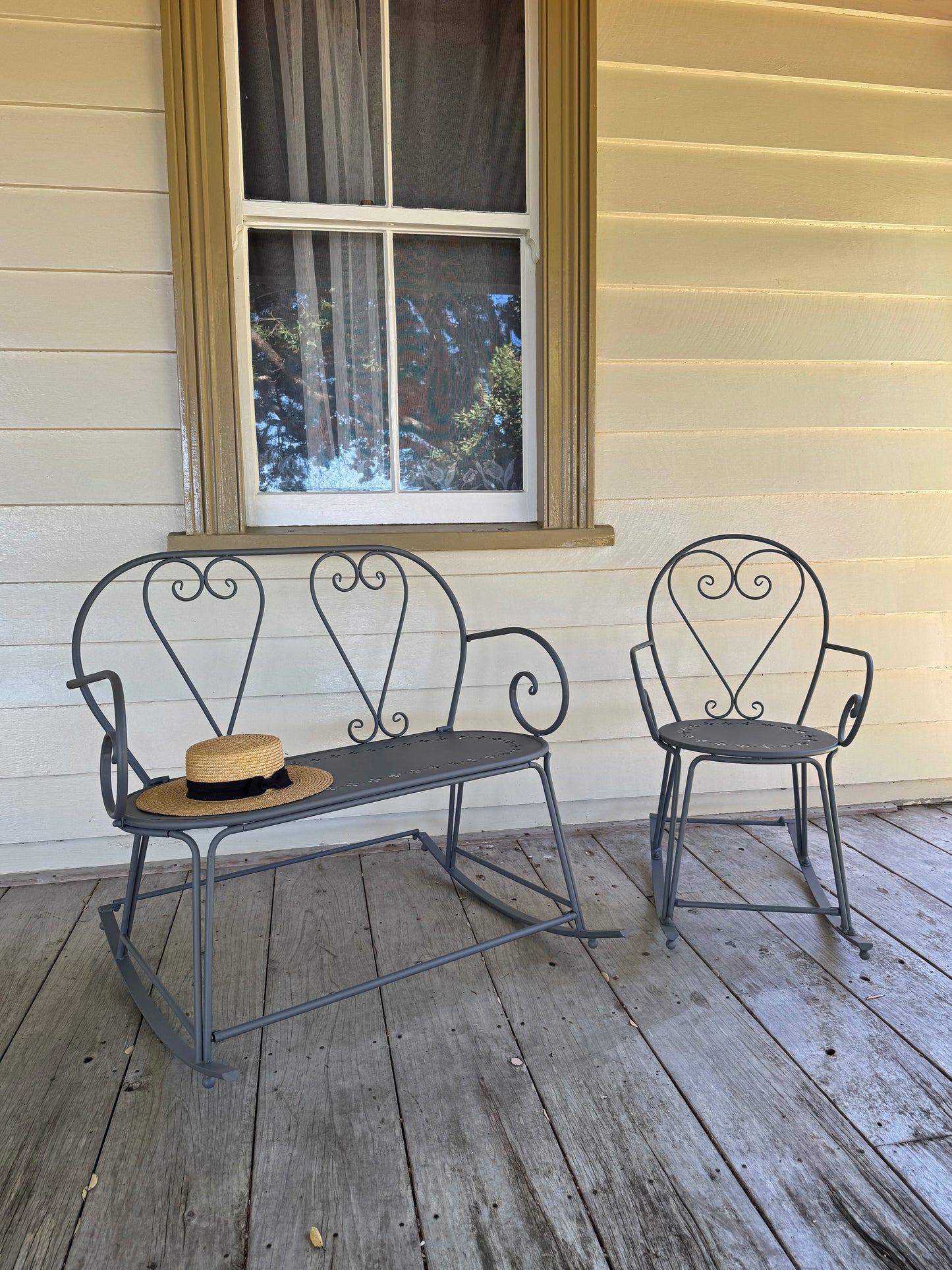 Metal bench and chair set on a wooden porch with a window in the background.