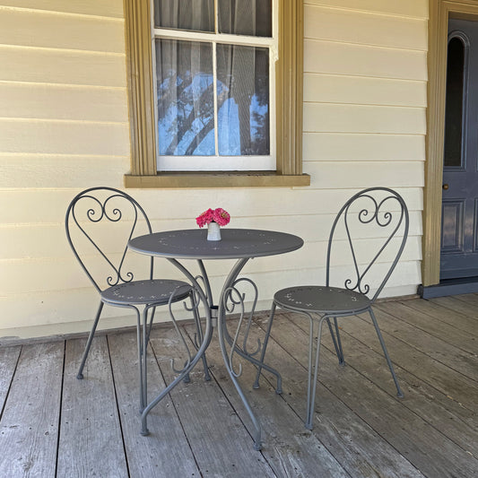 Outdoor setting with a small round table and two chairs on a wooden deck against a house.