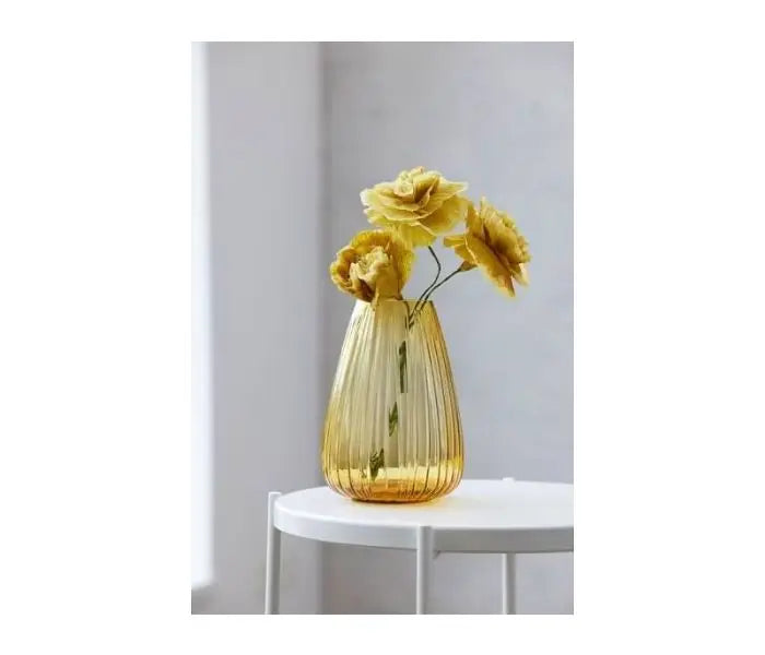 Yellow vase with flowers on a white table against a light gray wall