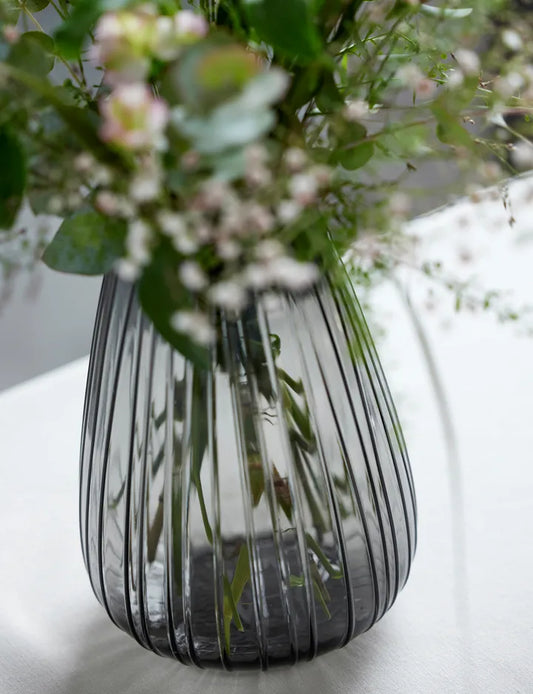 Striped glass vase with flowers on a white surface
