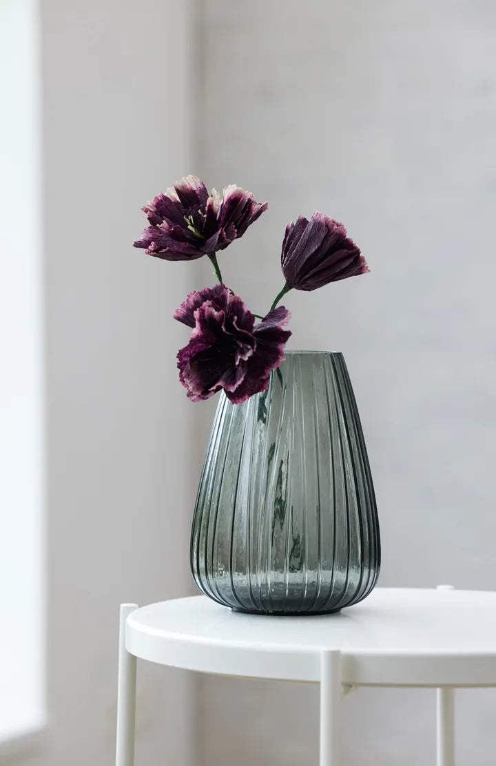 Glass vase with purple flowers on a white table against a light gray wall