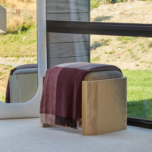 Wooden ottoman with a maroon blanket draped over it, set against a scenic outdoor background.