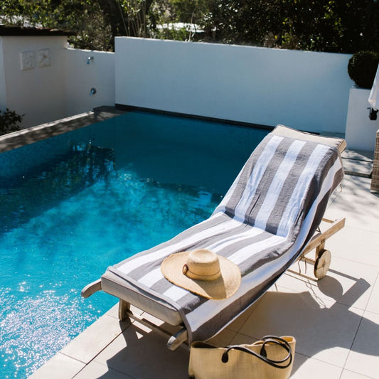 Chaise lounge with striped towel and straw hat by a pool