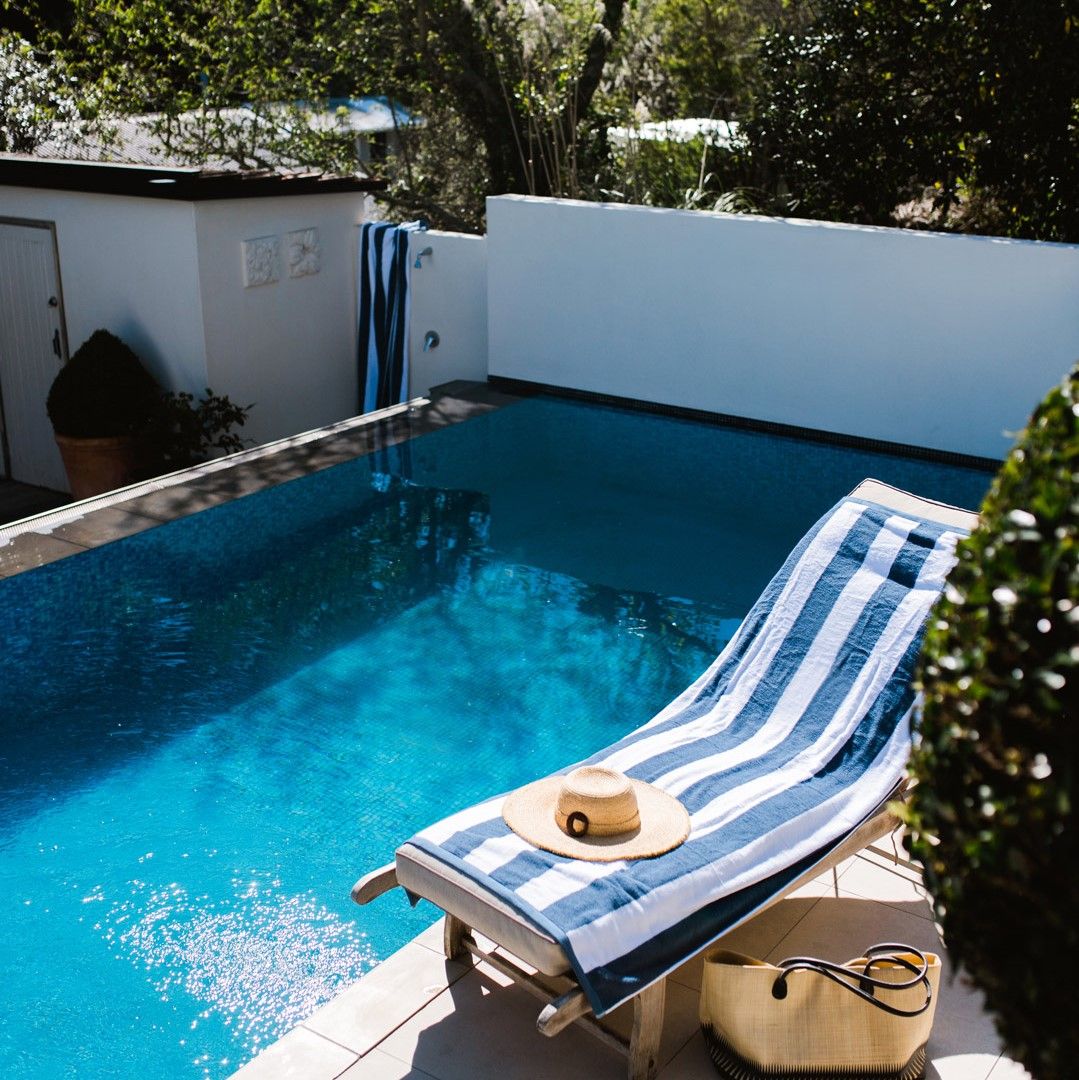 Poolside scene with a striped towel and hat on a lounge chair by a pool.