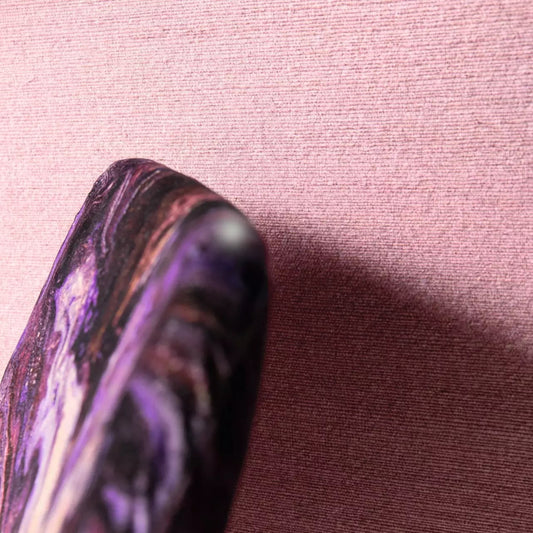 Close-up of a purple and black marbled object on a pink fabric background