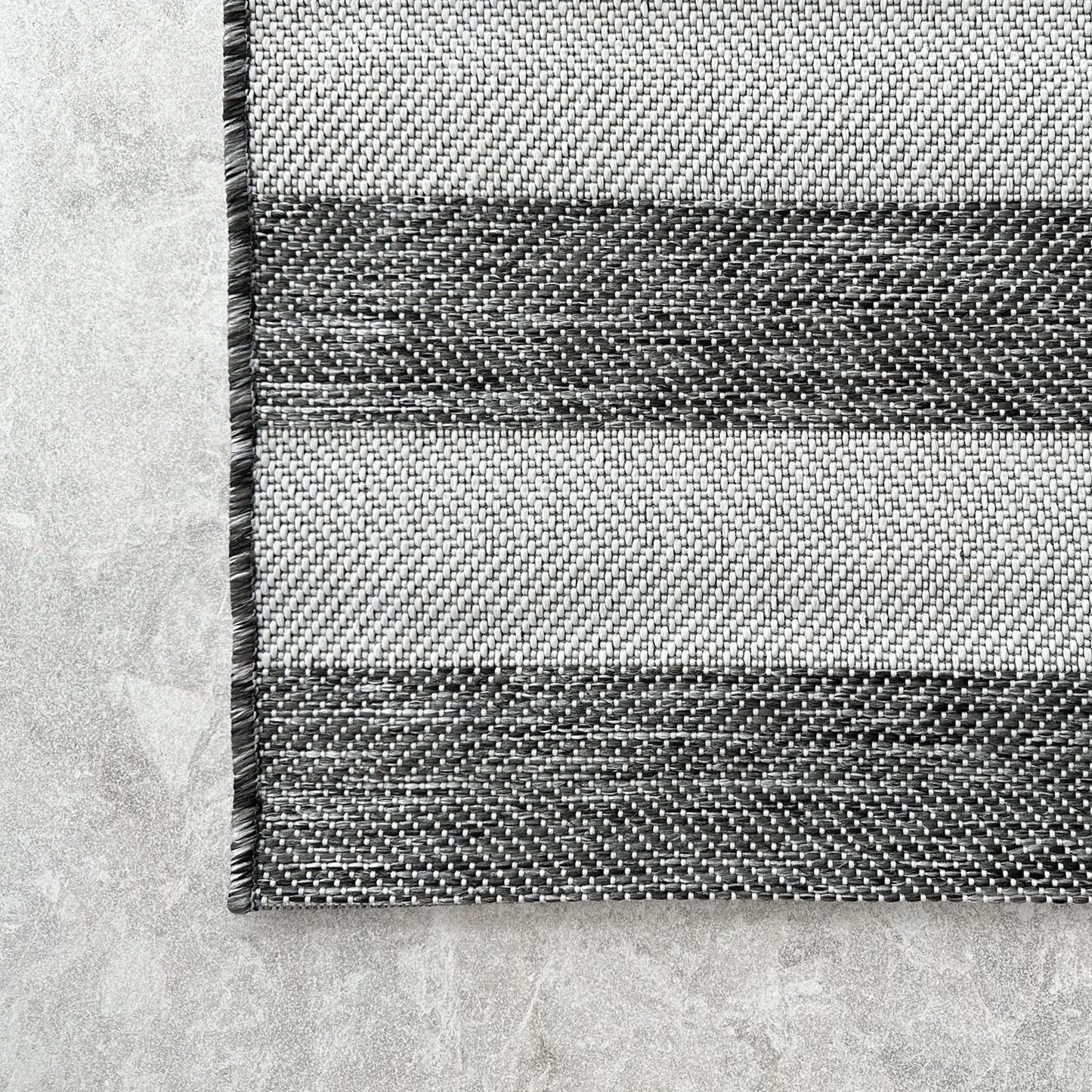 Close-up of a black and white striped rug on a concrete floor