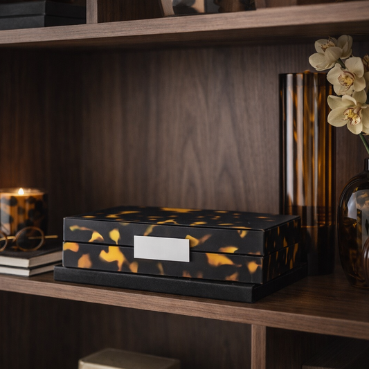 Decorative box with gold accents on a wooden shelf with books and a vase.