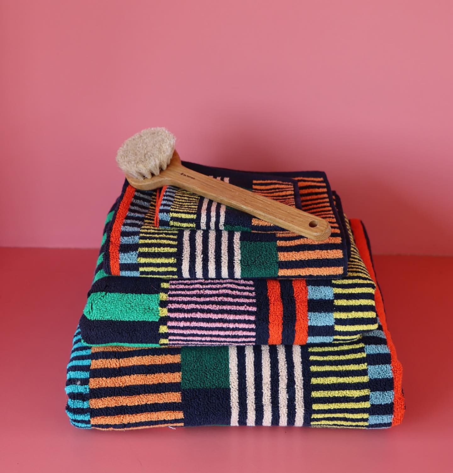 Colorful textured towel with a scrub brush on a pink background