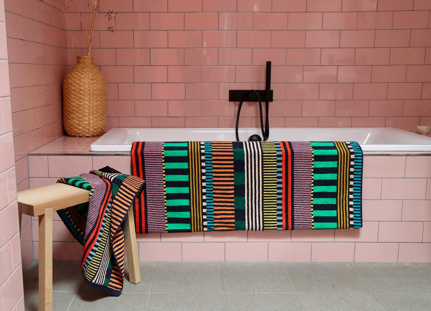 Colorful striped towel draped over a bathtub in a bathroom with pink tiled walls.