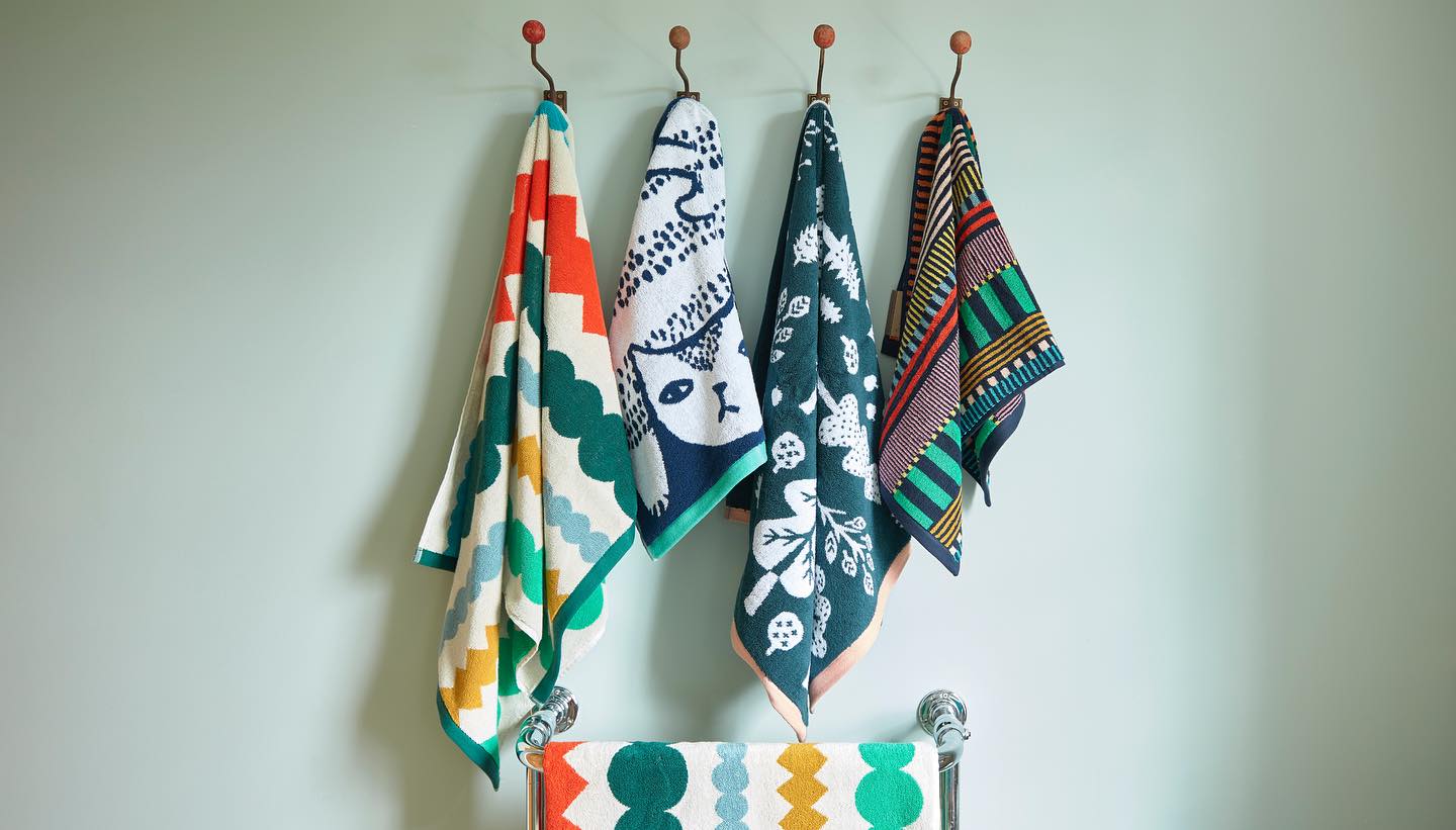 Colorful patterned towels hanging on a rack against a light gray wall.