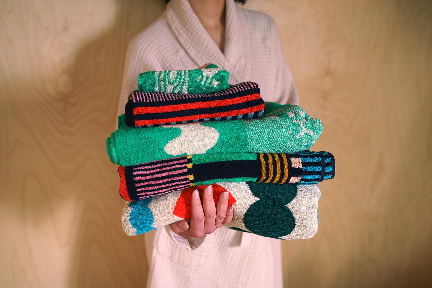 Person holding a stack of colorful patterned towels against a wooden background