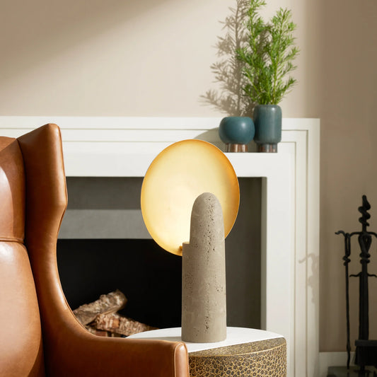 Cylindrical table lamp with a textured base on a side table next to a brown armchair.