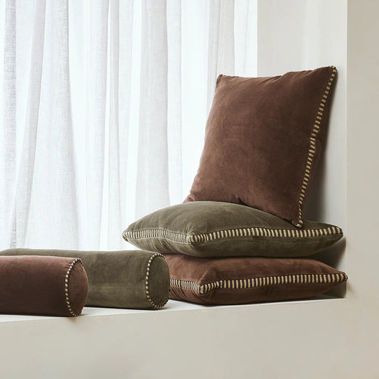 Brown and green cushions on a light surface with white curtains in the background