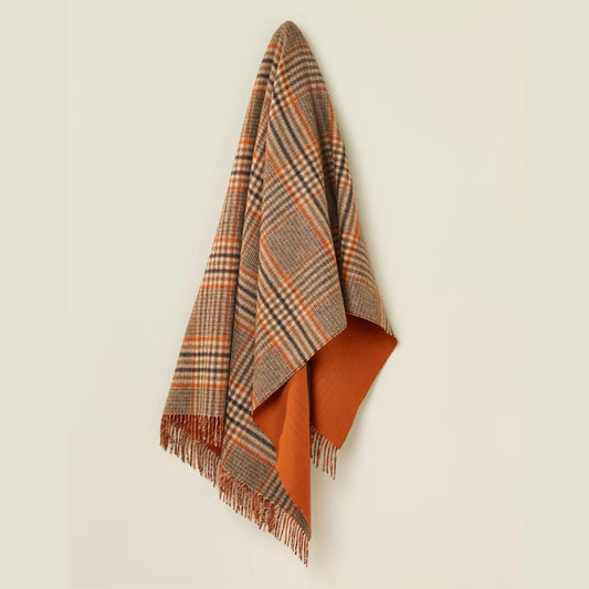 Plaid blanket with orange and brown colors draped over a light beige background