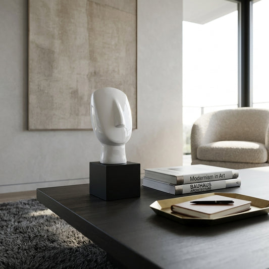A white sculptural head sculpture on a black pedestal, styled on a dark wooden coffee table in a modern living room setting.