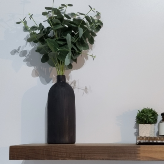Floating shelf in walnut with a black vase filled with eucalyptus leaves