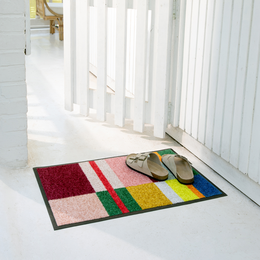 Colorful doormat with a geometric pattern on a white floor, featuring two shoes.