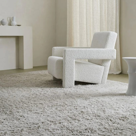 soft textured pale grey plain rug with wihite boucle modern uphostered chair, white wood plain fireplace in the backgroundwith white vases on against a while wall, with white linen curtains closed
