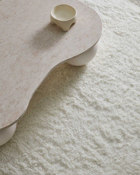 Textured ivory coloured carpet with a corner shot of a stone coffee table with a pot on