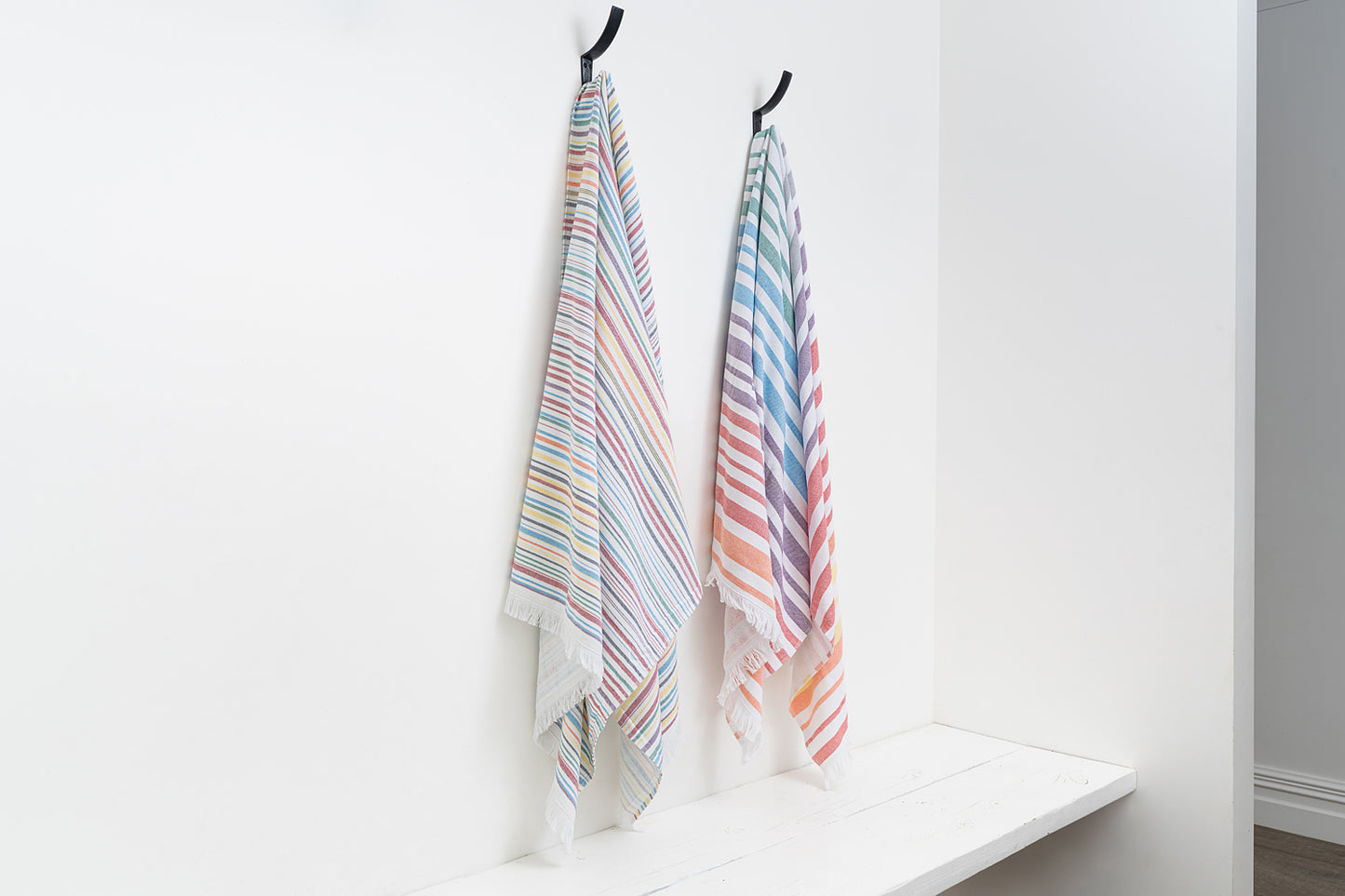 Two striped towels hanging on a white wall with a shelf.
