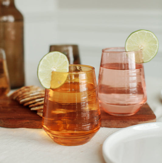 Two water tumblers with lime slices on a wooden coaster on a white surface.