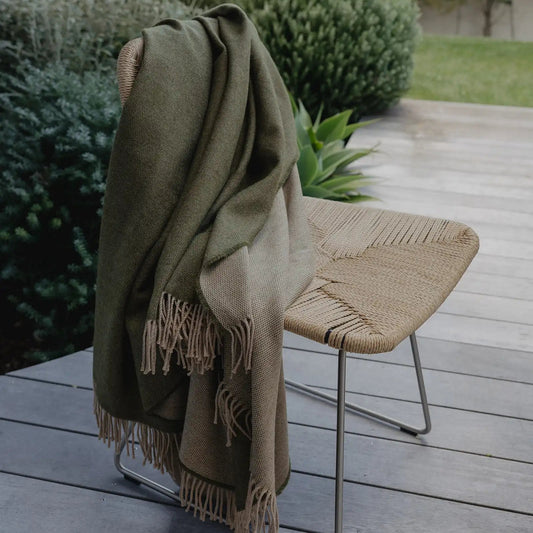 Green blanket draped over a chair on a wooden deck with plants in the background
