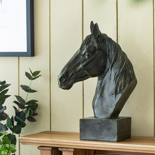 Black horse head sculpture on a wooden shelf with a light green wall and plant in the background