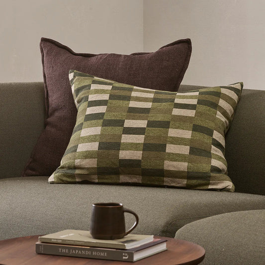 Plaid pillow on a sofa with a cup and books on a small table.