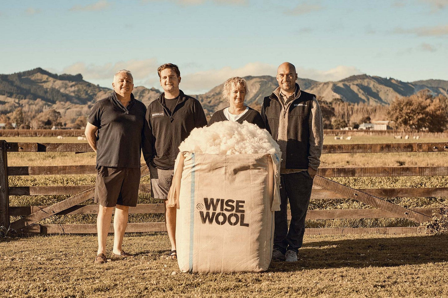 Four people standing with a large bag of Wise Wool in a pastoral setting.