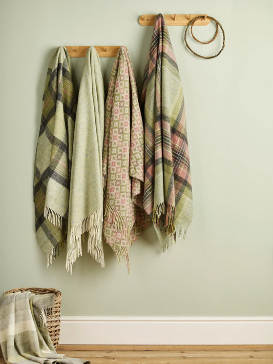 Plaid blankets hanging on a wooden rack against a light green wall.