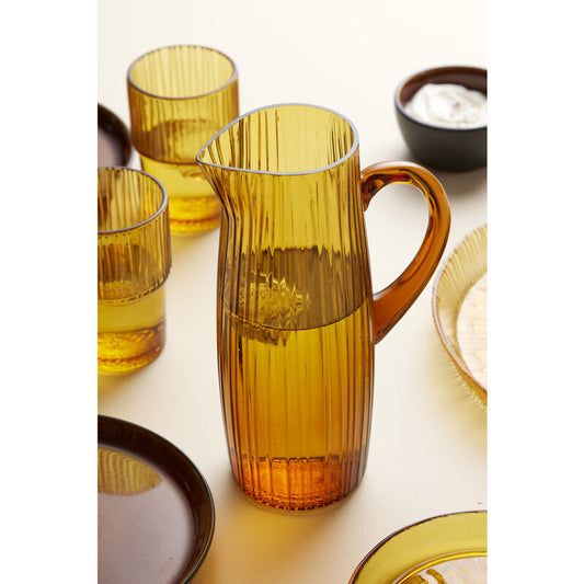 Set of amber glass tumblers and a pitcher on a white surface