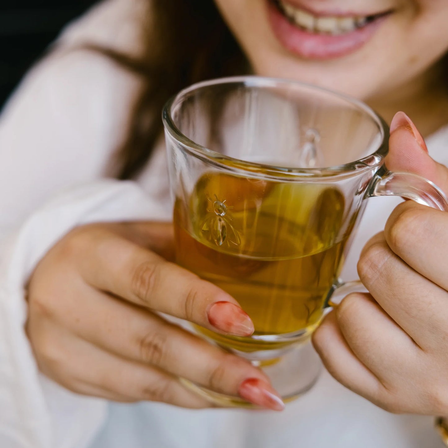 Person holding a clear mug with a warm beverage, possibly tea or coffee.