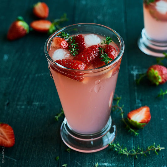 Glass of pink strawberry cocktail with ice and thyme on a dark wooden surface.