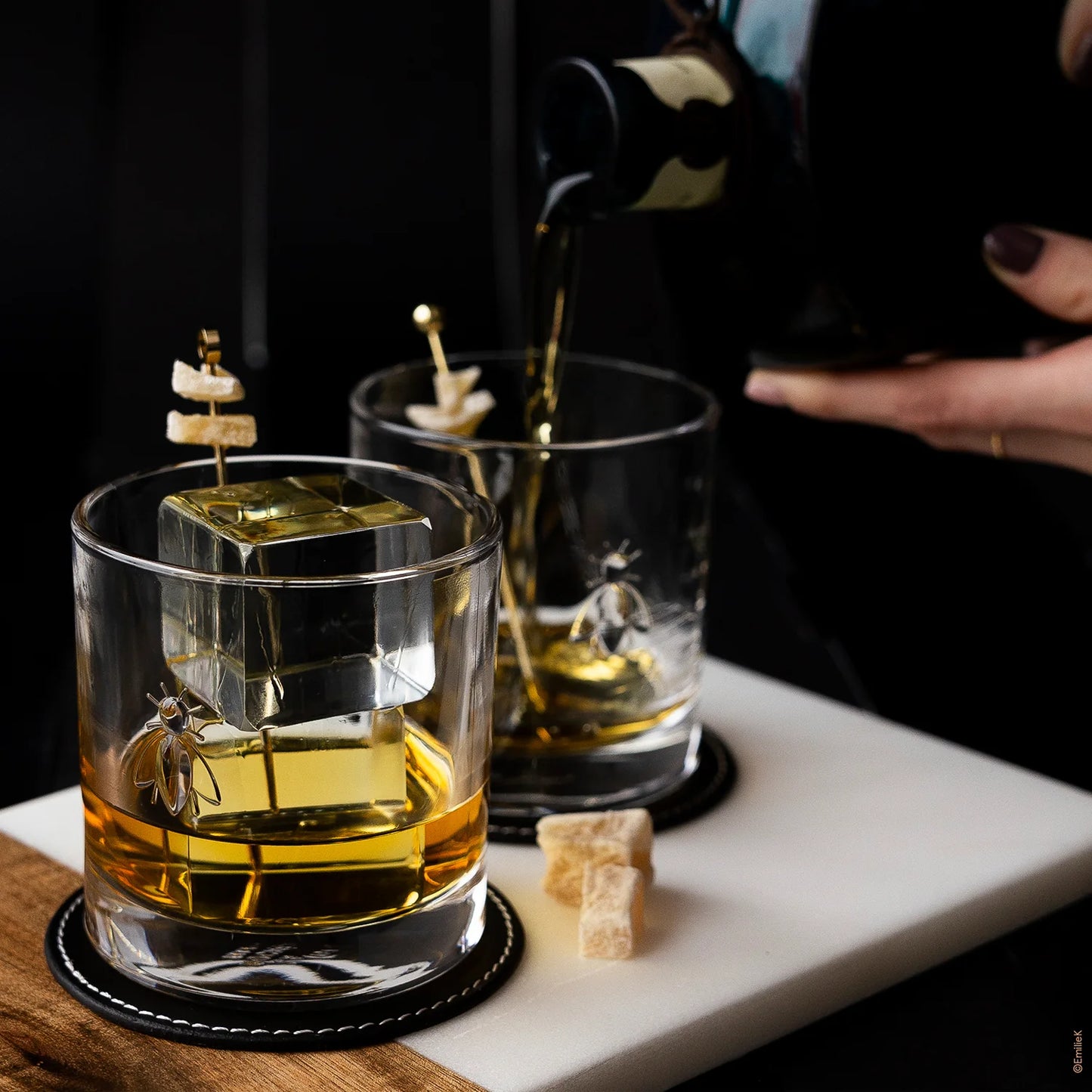 Two glasses with ice cubes and a ship design, one being filled with liquid on a dark background.