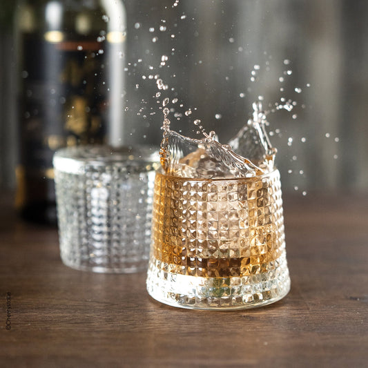 Glass with liquid splashing out, blurred bottle in the background