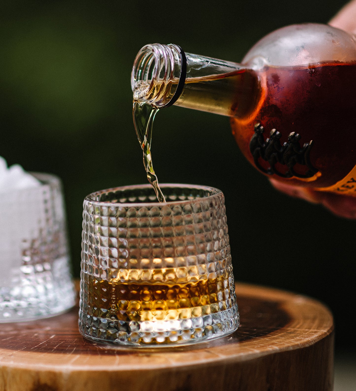 Bottle pouring liquid into a textured glass on a wooden surface