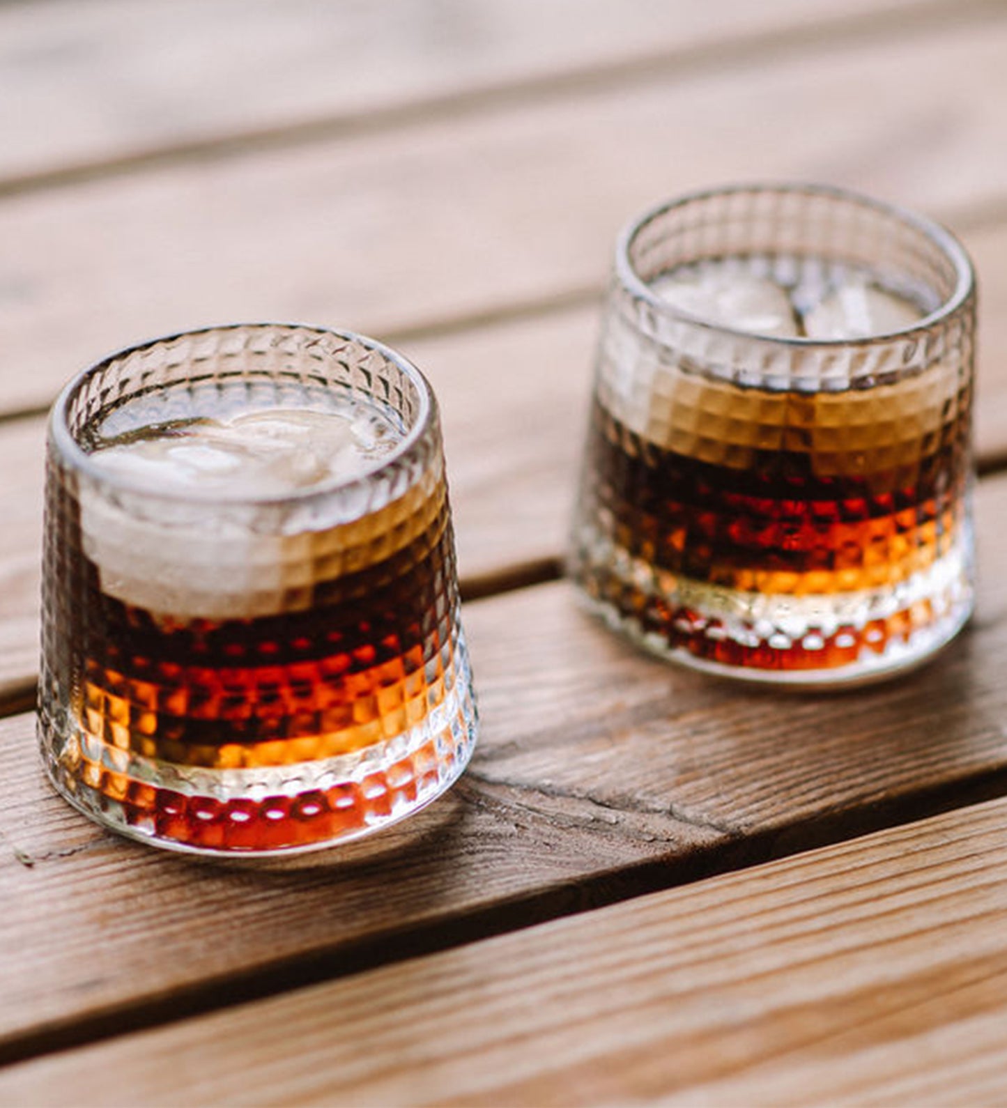 Two glasses of layered drinks on a wooden surface