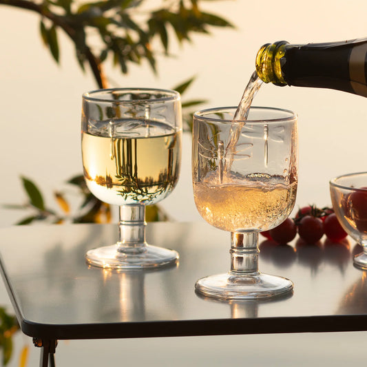 Wine being poured into a glass on a table with grapes and a blurred natural background