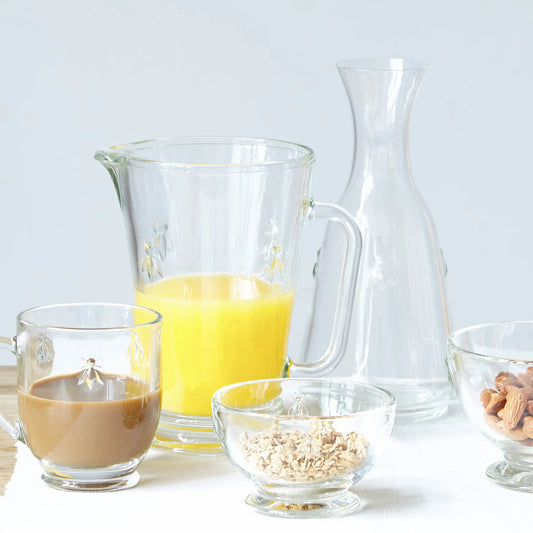 Clear glassware including a pitcher, cups, and bowls with various contents on a light background