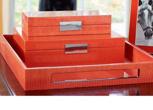 Set of orange decorative boxes with silver handles on a reflective surface.