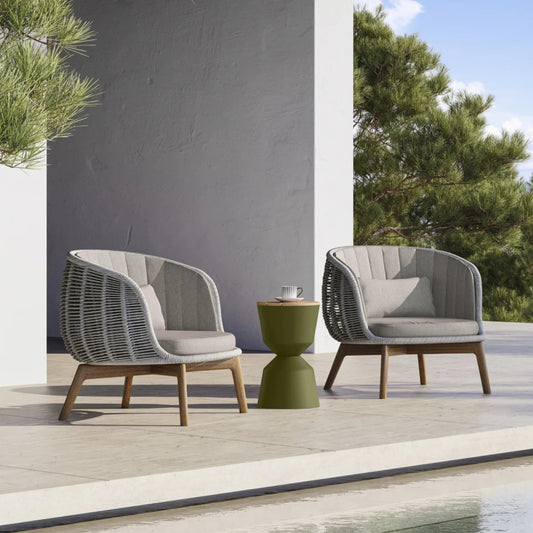 Modern outdoor furniture set with two chairs and a small table on a patio with trees and pool in the background.