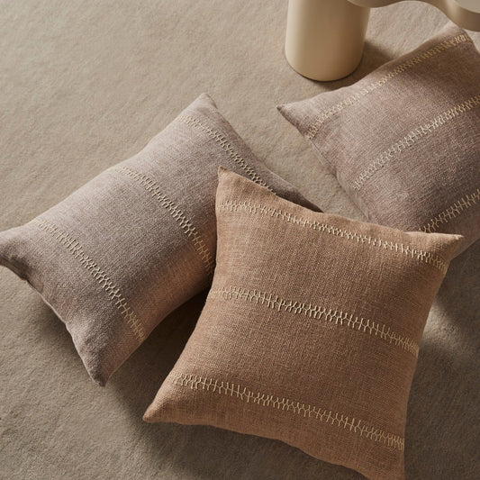 Three beige pillows on a textured surface with a cylindrical object in the background.