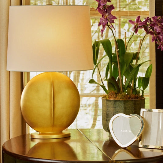 Mariza round table lamp in gold, manufacturer AERIN on a table