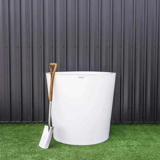 White fire pit with a shovel on green grass against a dark metal wall