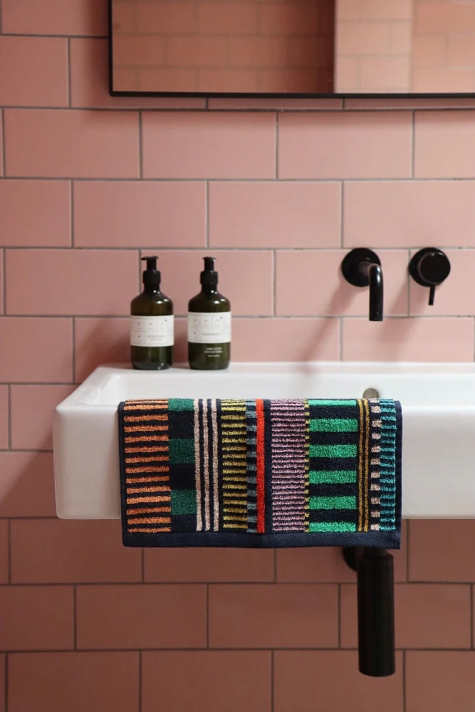 Bathroom sink with bottles and a colorful towel on a pink tiled wall.