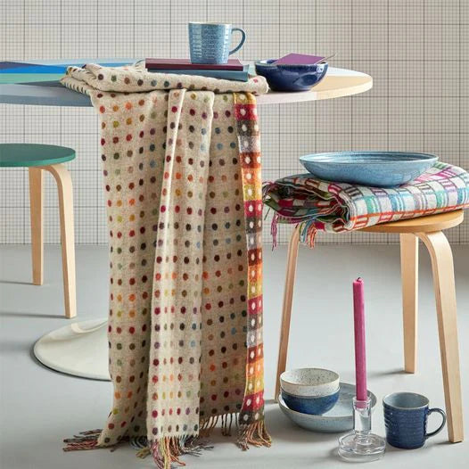 Colorful polka dot scarf draped over a table with bowls and mugs in a home setting.