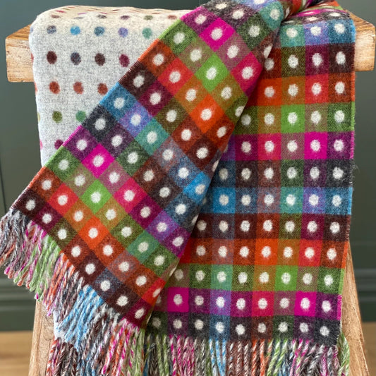 Colorful polka dot blanket with fringe on a wooden stool against a dark background